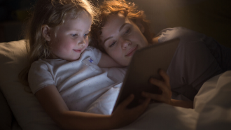 mother and child laying in bed watching something on an ipad