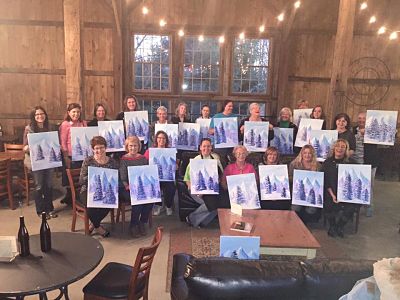 Group of women standing in a row holding up canvases featuring winter trees