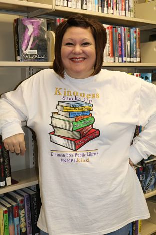 Woman smiling standing and leaning against a book shelf